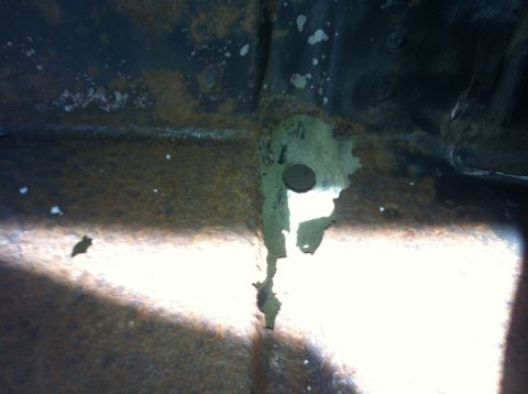 1979 Ford Bronco - This image shows a close-up view of heavily rusted and corroded metal, likely a vehicle frame or undercarriage, with a hole exposing a ligh…