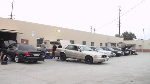 2003 Ford Crown Victoria - Photograph of several sedans with hoods up parked outside an automotive shop, not a technical document.