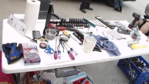 2003 Ford Crown Victoria - folding table is spread with sockets, screwdrivers, pliers, scissors and a red Performance-branded box during an outdoor work session.