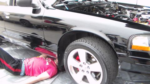 2003 Ford Crown Victoria - Photograph of a person on the ground servicing a black car at the front wheel, not a technical document.