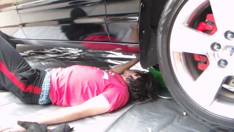 2003 Ford Crown Victoria - Photograph of a person working underneath a black car near the front wheel, not a technical document.