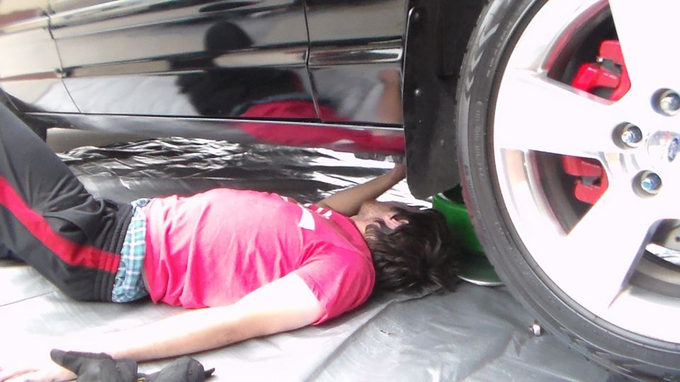 Person lying under a black sedan reaching behind the wheel