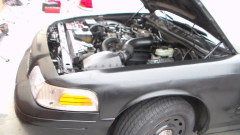 2003 Ford Crown Victoria - Photograph of the front and open engine bay of a black sedan in a garage, not a technical document.