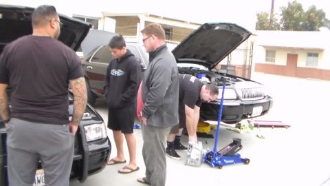 2003 Ford Crown Victoria - Photo of several people gathered around a car with the hood up and a blue floor jack, not a technical document.