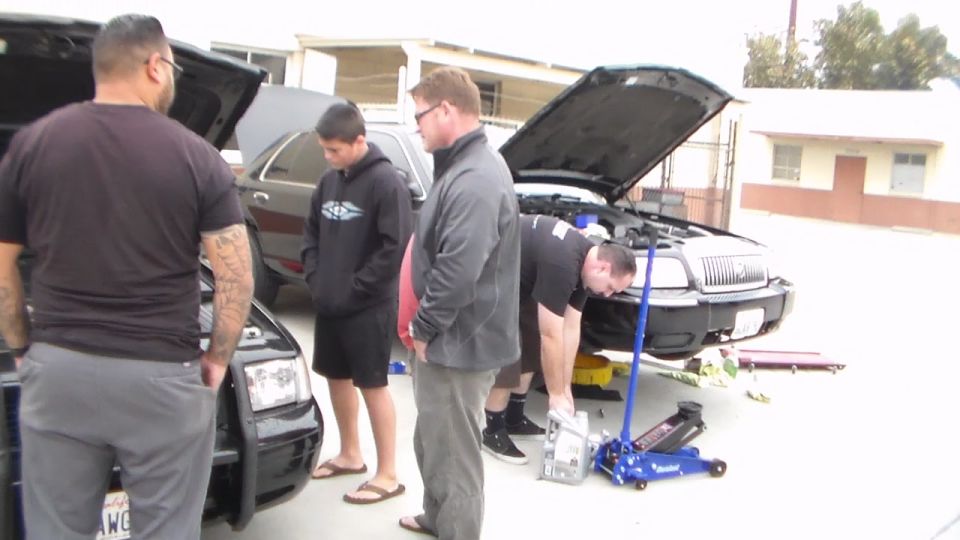 Group of people working on a car with floor jack in a lot