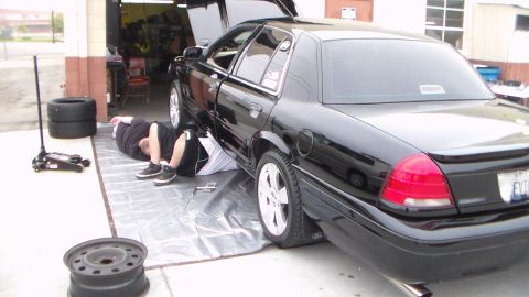 2003 Ford Crown Victoria - Photo of a black Ford Crown Victoria with someone lying under it and a spare wheel nearby, not a technical document.