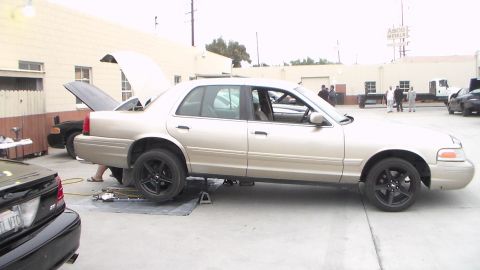 2003 Ford Crown Victoria - Photo of a gold Ford Crown Victoria raised on stands with hood open outside a shop, not a technical document.