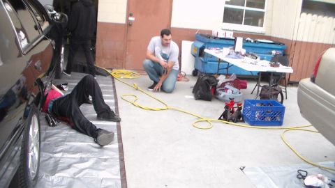 2003 Ford Crown Victoria - Photo of a work session with people, hoses, and tools on a shop floor next to cars, not a technical document.