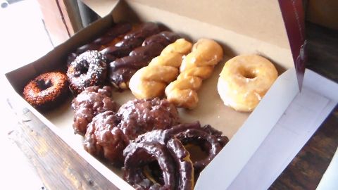 2003 Ford Crown Victoria - open cardboard box holds assorted donuts including chocolate-frosted, glazed rings, twists and fritters.
