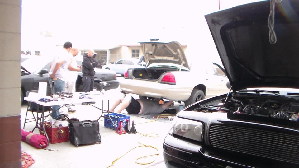 Black car with raised hood beside a silver Crown Victoria in a garage lot