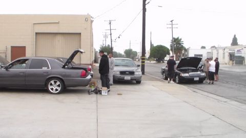 2003 Ford Crown Victoria - Photo of several cars lined along a street with trunk and hoods open, not a technical document.