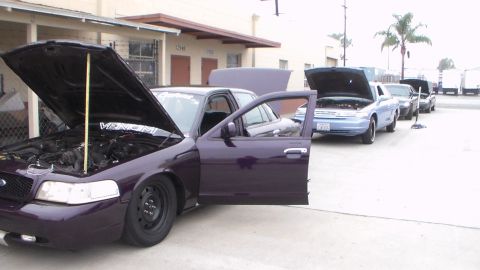 2003 Ford Crown Victoria - Photo of a purple Ford Crown Victoria with open hood and door parked with other cars, not a technical document.