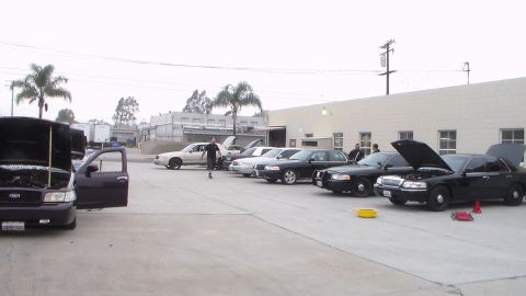 2003 Ford Crown Victoria - Photo of several sedans and a van parked in a shop lot with hoods open, not a technical document.