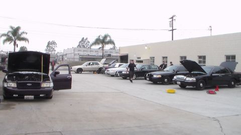 2003 Ford Crown Victoria - Photo of a row of cars with open hoods in a parking lot and a person walking, not a technical document.