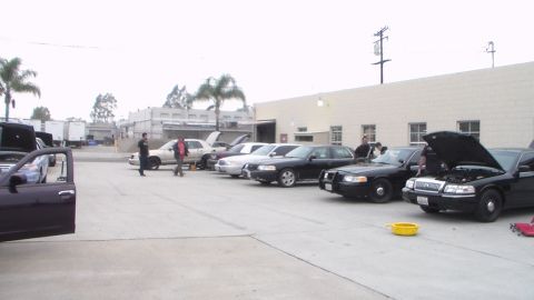 2003 Ford Crown Victoria - Photo of several cars with hoods open and people in a shop parking lot, not a technical document.