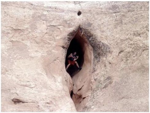 Person inside a cave opening in a rock formation.
