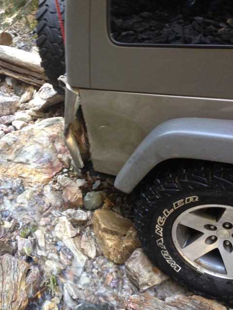 2005 Jeep Wrangler - The rear corner of a silver Jeep Wrangler is damaged, with the body panel torn open, revealing internal components. The vehicle is parked o…