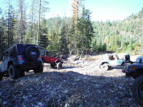 2005 Jeep Wrangler - Four Jeep Wranglers are parked on a rocky, wooded trail. The lead Jeep is dark gray, and three others are visible behind it, including a re…
