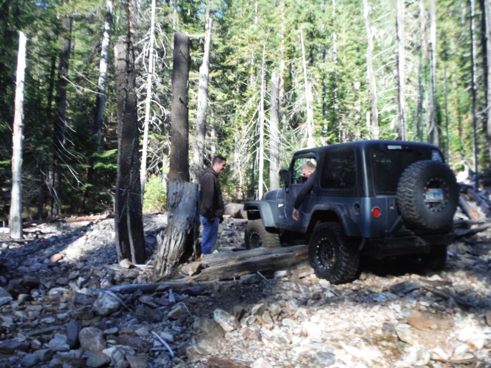 Dark blue 2005 Jeep Wrangler on a rocky forest trail with two people standing nearby