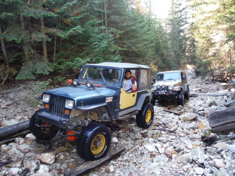Two Jeep Wranglers on a rocky trail; the front one is dark blue with yellow doors, the rear one is silver