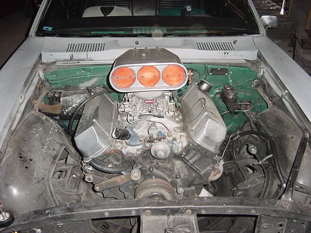 V8 engine with carburetor and tall three-filter orange air scoop in a stripped white vehicle's engine bay