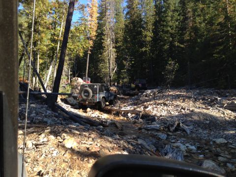 2005 Jeep Wrangler - A silver Jeep Wrangler navigates a challenging, debris-strewn forest path with another vehicle visible in the distance.