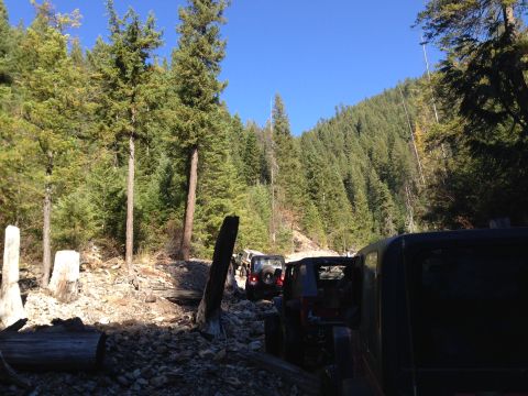 2005 Jeep Wrangler - Multiple Jeeps navigate a challenging, rocky path through a dense forest under a clear blue sky.