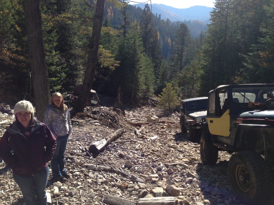 Yellow Jeep Wrangler and a dark Jeep parked on a rocky, wooded trail