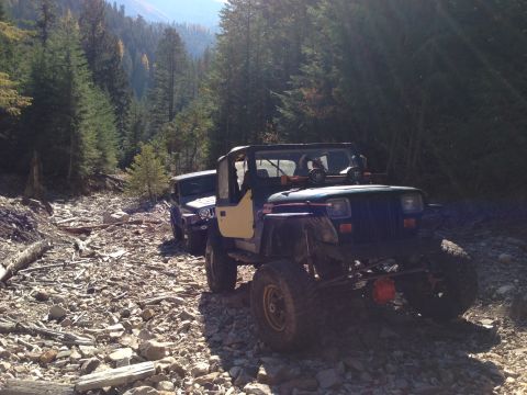 2005 Jeep Wrangler - Two Jeep Wranglers navigate a rocky, wooded trail under a bright sky.