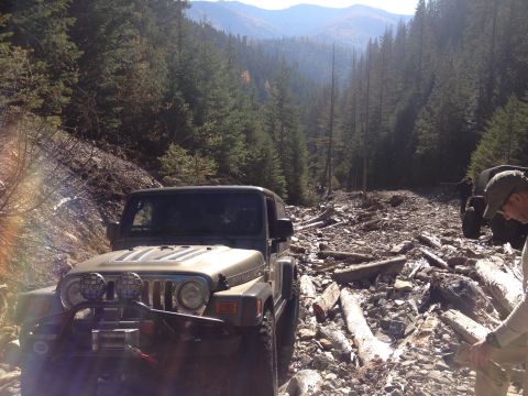 2005 Jeep Wrangler - A Jeep Wrangler navigates a rough, rocky mountain path surrounded by dense forest.