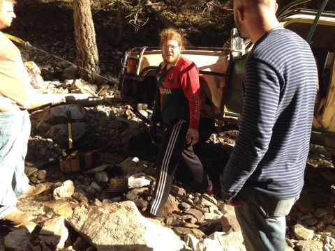 2005 Jeep Wrangler - Several people are gathered around a vehicle that appears to be stuck in a rocky, wooded area.