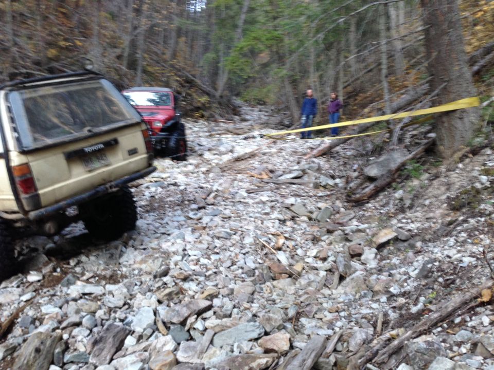 Tan Toyota pickup truck and red Jeep Wrangler on a rocky trail. Toyota badge visible