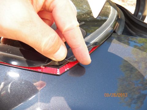 1998 Lincoln Mark VIII - Adhesive backing is being removed from a black trim piece, likely for installation on a vehicle's rear window seal.