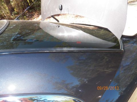 1998 Lincoln Mark VIII - The rear window seal of a dark gray car is visible with the hood open in the background.