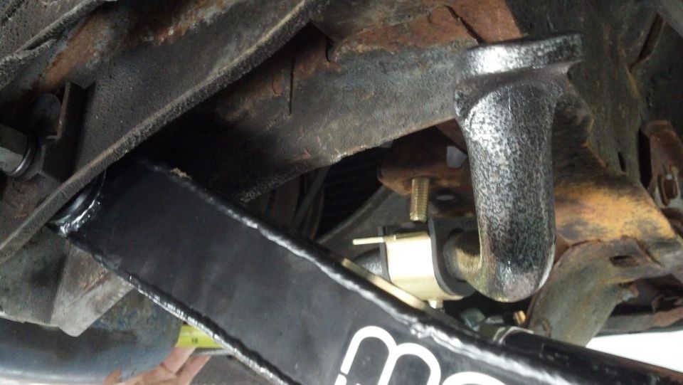 Close-up of a vehicle's suspension component, possibly a shock absorber mount, with visible rust on the frame