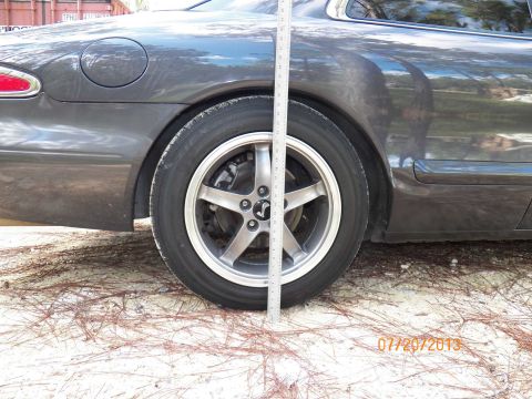 1998 Lincoln Mark VIII - A ruler is used to measure the ride height of a dark gray coupe. The vehicle's specific year and model are not identifiable from this image.