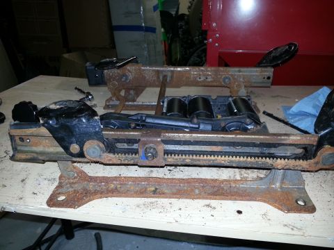 1994 Ford Bronco - Two heavily rusted seat rail assemblies with black plastic components and metal gears are shown on a workbench.