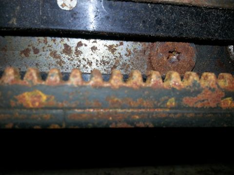 1994 Ford Bronco - Close-up view of a heavily rusted seat mechanism, showing the gear teeth and a screw head.
