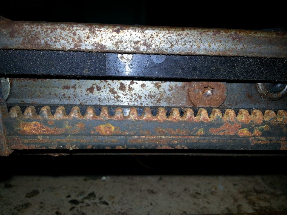 Close-up of a rusted metal seat adjustment mechanism with visible gear teeth and a black rubber strip