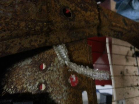 1994 Ford Bronco - Close-up of a heavily rusted metal bracket with visible fasteners and some red components in the background.