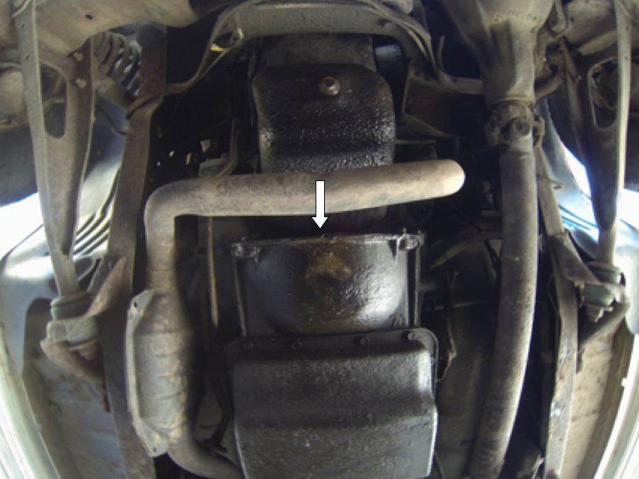 Underside view of vehicle showing exhaust pipe, catalytic converter, and oil pan. Arrow points to oil pan