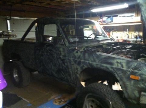 1975 Ford Courier - A pickup truck with a camouflage paint job is parked in a garage with its hood open.