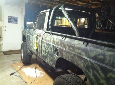 1975 Ford Courier - Camouflaged 1975 Ford Courier pickup truck with a roll bar and lifted suspension is parked indoors.