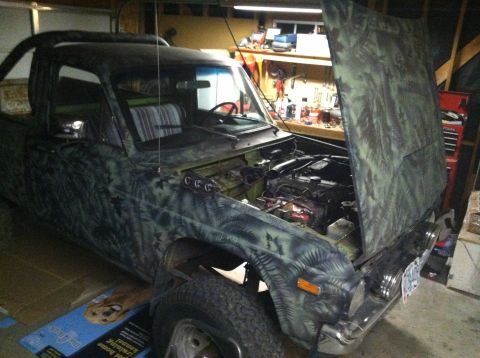 1975 Ford Courier - A camouflaged pickup truck is shown with its hood open in a garage, revealing the engine compartment and interior.
