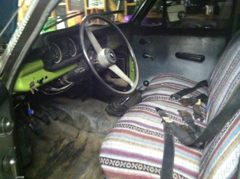 1975 Ford Courier - The interior of an older truck shows a steering wheel, dashboard, and seats with a distinctive woven pattern.