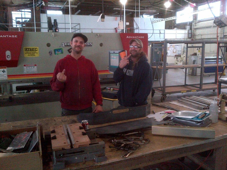 Two men in a workshop, one giving the middle finger.