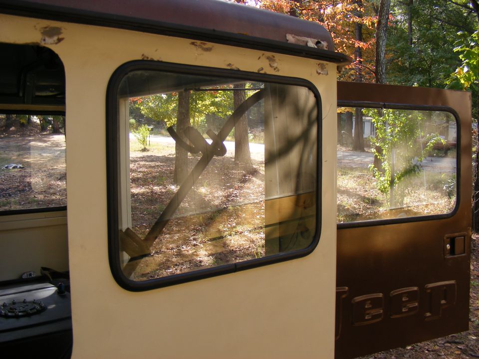 Side view of a Jeep CJ-7 interior, showing the door and window. Trees and foliage visible outside