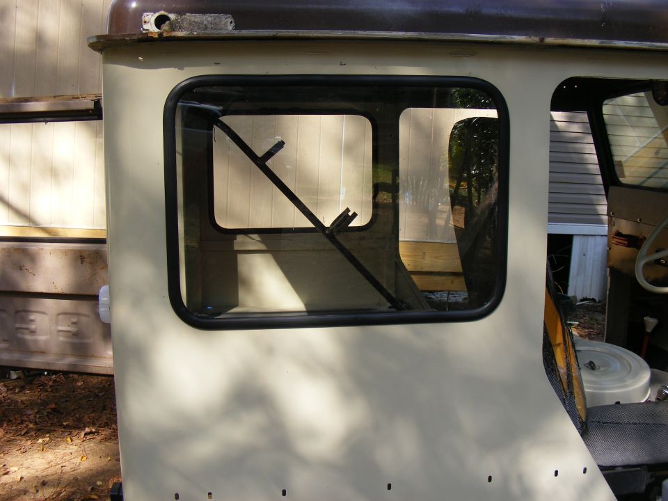 Cream-colored vehicle cab side with a split window frame and dark tint. A metal bar is visible inside