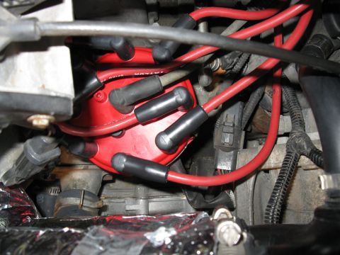 1996 Ford Bronco - Close-up view of red spark plug wires and a red distributor cap within an engine bay.
