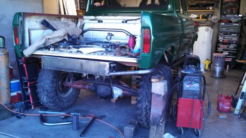 1967 Ford F-250 - A green pickup truck is shown in a garage, undergoing modifications with a large fuel tank installed under the bed.